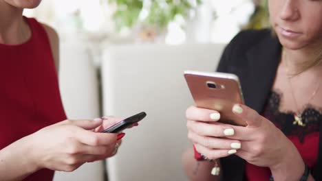 Two-young-girlfriends-using-smartphone-and-talking-in-cafe-and-drinking-coffee.-Shot-in-4k