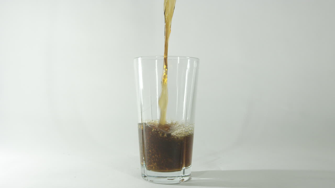 filmati al rallentatore di cola che viene versata in un bicchiere su uno sfondo chiaro e chiaro
