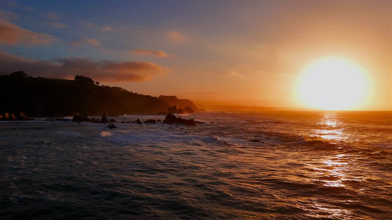 Ampia vista sull'oceano con tramonto luminoso e costa frastagliata in lontananza