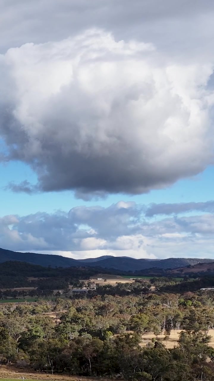 Una enorme nube blanca flota sobre colinas ondulantes y matorrales en una composición de paisaje vertical