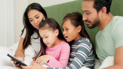 mother, father and children on bed with a tablet