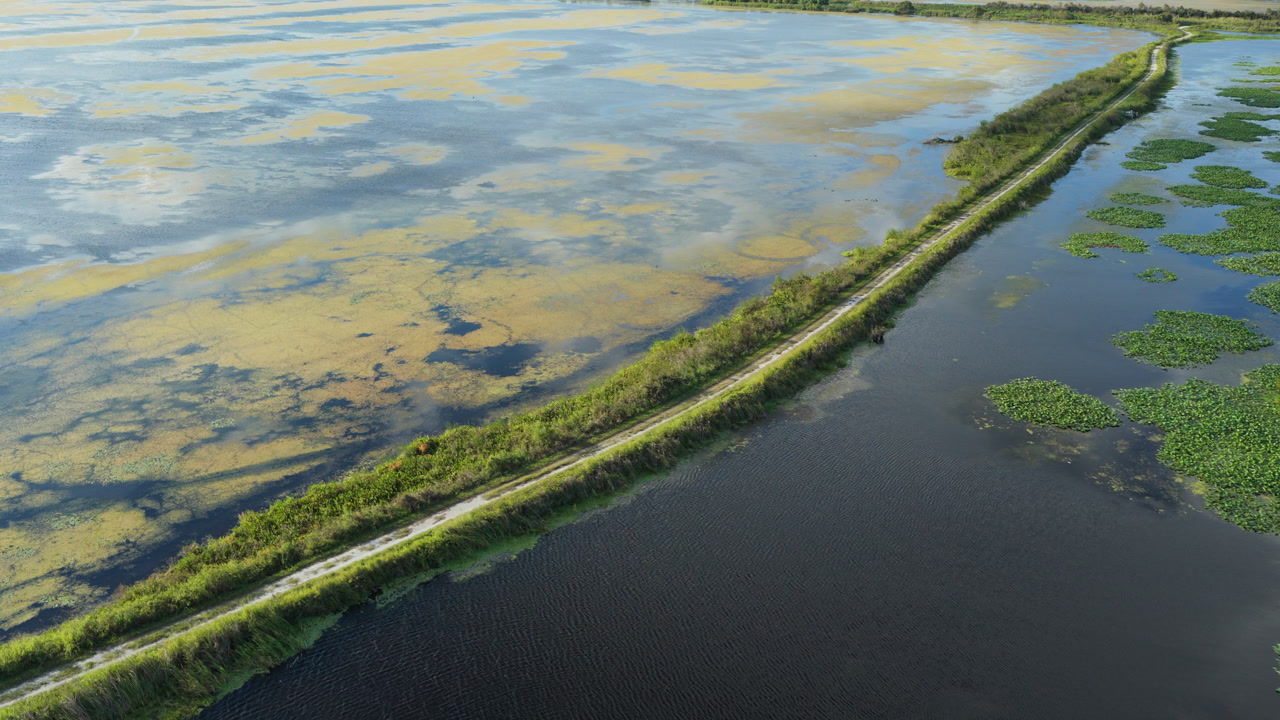 Aerial angled dolly across marsh waterway with floating vegetation patches reflecting cloudy sky Emeralda Marsh Florida