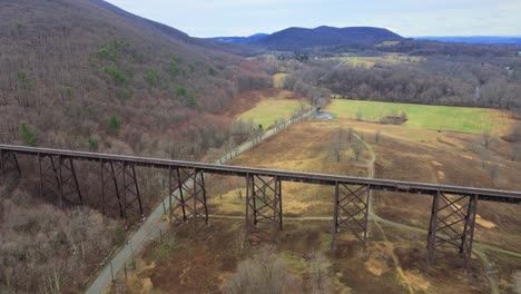 aerial drone video footage of a train bridge viaduct running over a valley in the appalachain mountains during early spring on a cloud day, surrounded by mountains and farmland