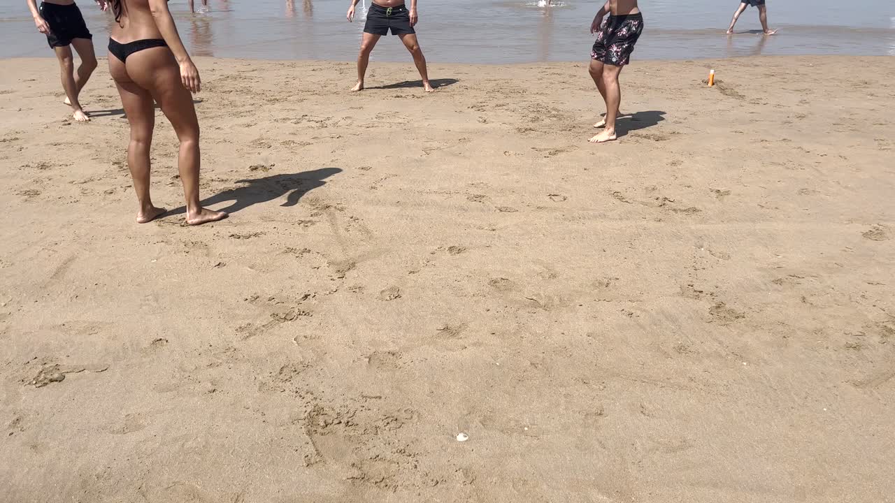 задний вид красивой счастливой загорелой женщины в черном бикини, играющей или бегущей возле кораблекрушения на пляже во время захода солнца - видео в замедленном движении