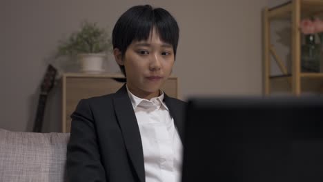 closeup sleepy asian businesswoman sitting behind computer is waking with a start and rubbing her eyes while working late on couch in the living room at home.