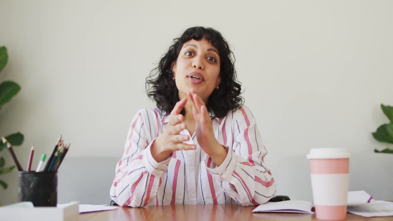 feliz mujer biracial sentada en el escritorio hablando y sonriendo durante la videollamada