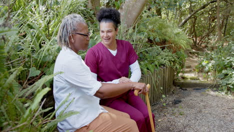 carer holding hands with elderly person, sitting on bench in garden