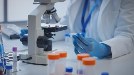 primer plano de un trabajador de laboratorio que lleva a cabo investigaciones utilizando un microscopio con un tubo de ensayo etiquetado phi