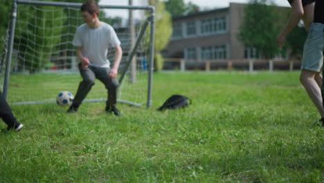 a family engages in a fun outdoor soccer game as a boy in a red shirt places the ball into the net, the goalkeeper, missing the save, playfully sits on the ball while watching it roll into the goal