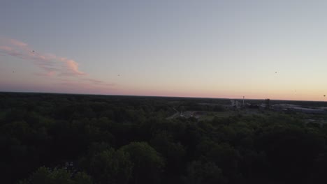 Drone dolly motion at dusk with silhouette over small village

Drone shot with dolly movement at dusk with silhouette over small village in well wooded place