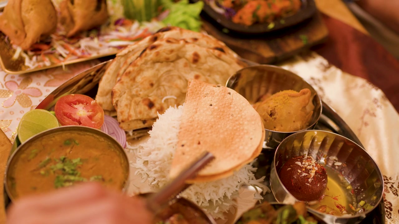 Overhead view of hand placing papadum on metal plate with assorted Indian dishes.