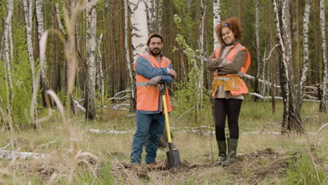 activista afroamericana y compañera de trabajo árabe posando para la cámara en el bosque mientras ella cruza los brazos y él sostiene una pala