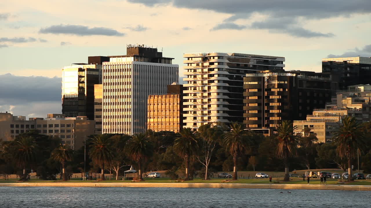 Modernos edificios de apartamentos con vista al lago, atardecer dorado reflejado sobre el tráfico y los paseantes abajo