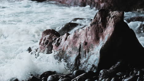 slow motion shot of strong waves crashing against red and black colored basalt rocks at hawaiian coast