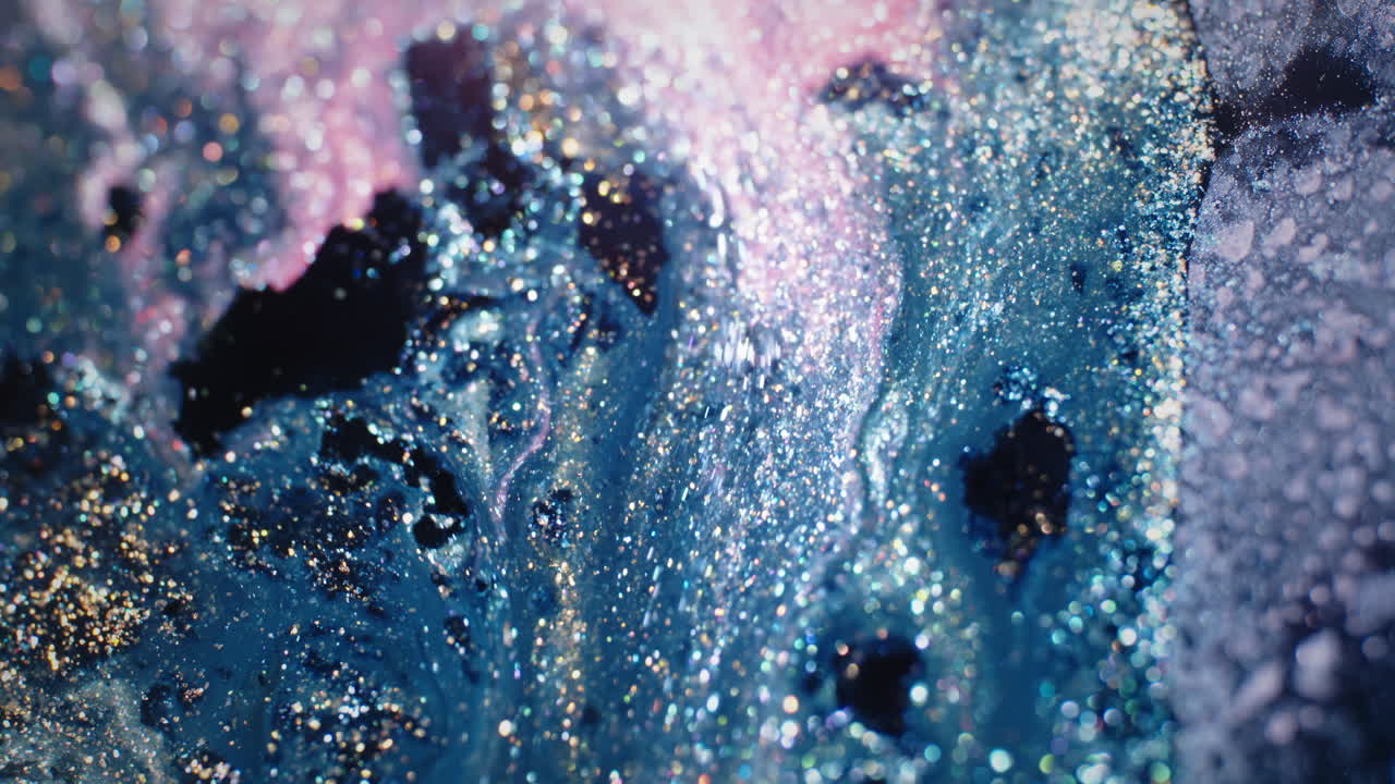 Swirling blue and black pigments blend with glitter in a mesmerizing macro shot of mixed substances