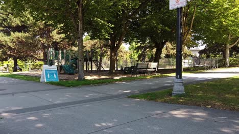 Leerer-Uniblock-Gehweg-Park-Kinderspielplatz-Mit-Niemand-Draußen-Während-Der-Lockdown-beschränkung-Pandemie-Covid-19-Vintage-Lichtpfosten-Bänke-üppig-Grüne-Waldzeltzeichen-Soziale-Distanzierung