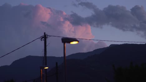 close-up-street-lamp-at-late-afternoon,-big-pink-clouds-in-the-background,-occasional-lightning-flash-in-the-distance