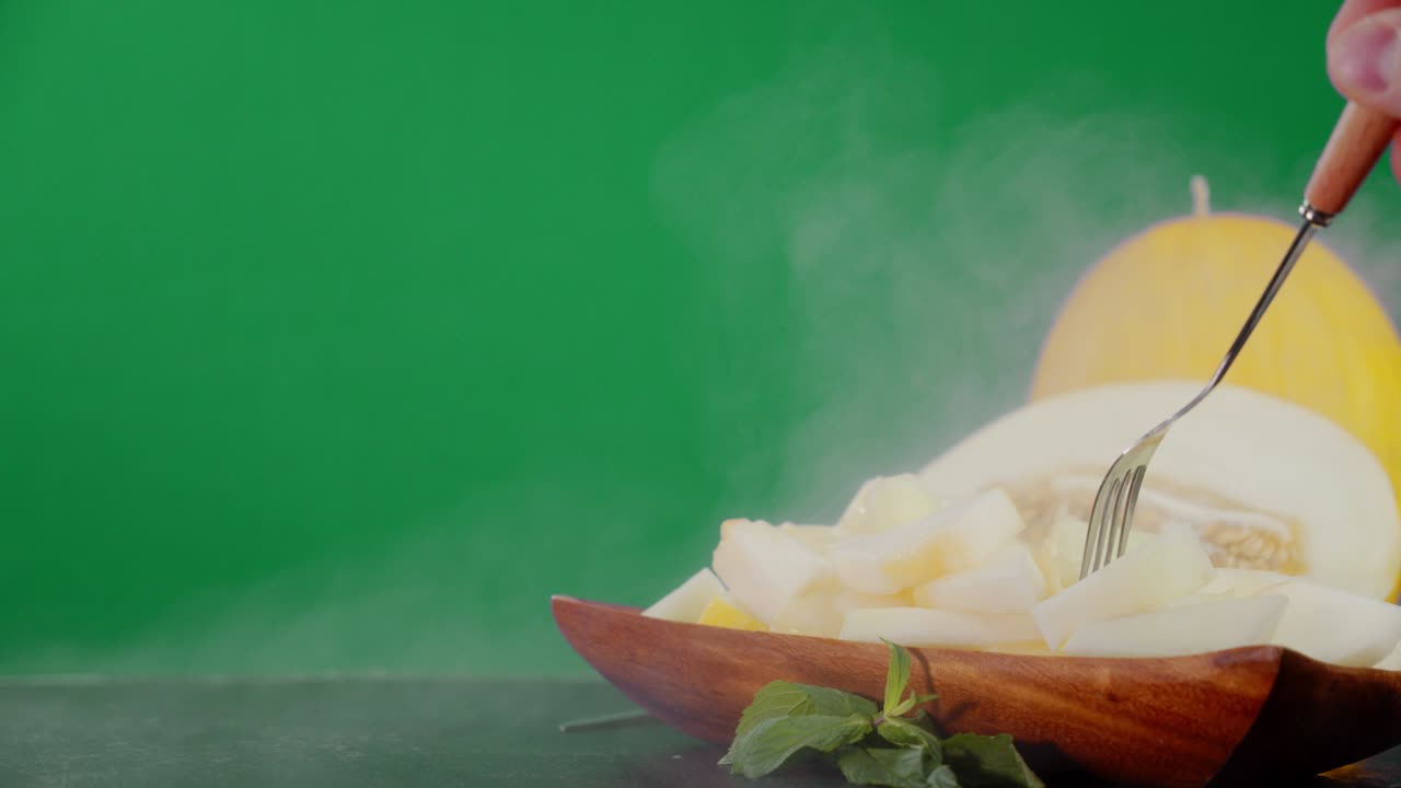 Male hand with fork takes a piece of melon from the plate.