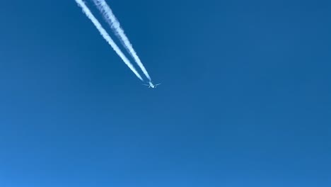 POV-aerial-shot-of-a-white-fuselage-jet-and-its-wake-crossing-a-turquoise-sky-shot-from-another-jet-flying-bellow