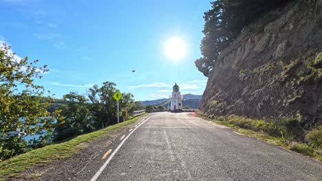 a serene drive along a coastal road in akaroa, new zealand, with a lighthouse in view under bright morning sunlight