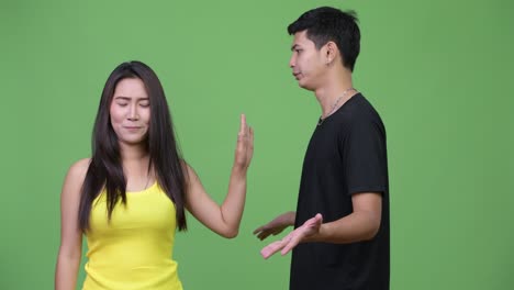 젊은 아시아 여성이 젊은 분노한 아시아 남자에게 멈추는 몸짓을 보여줍니다.