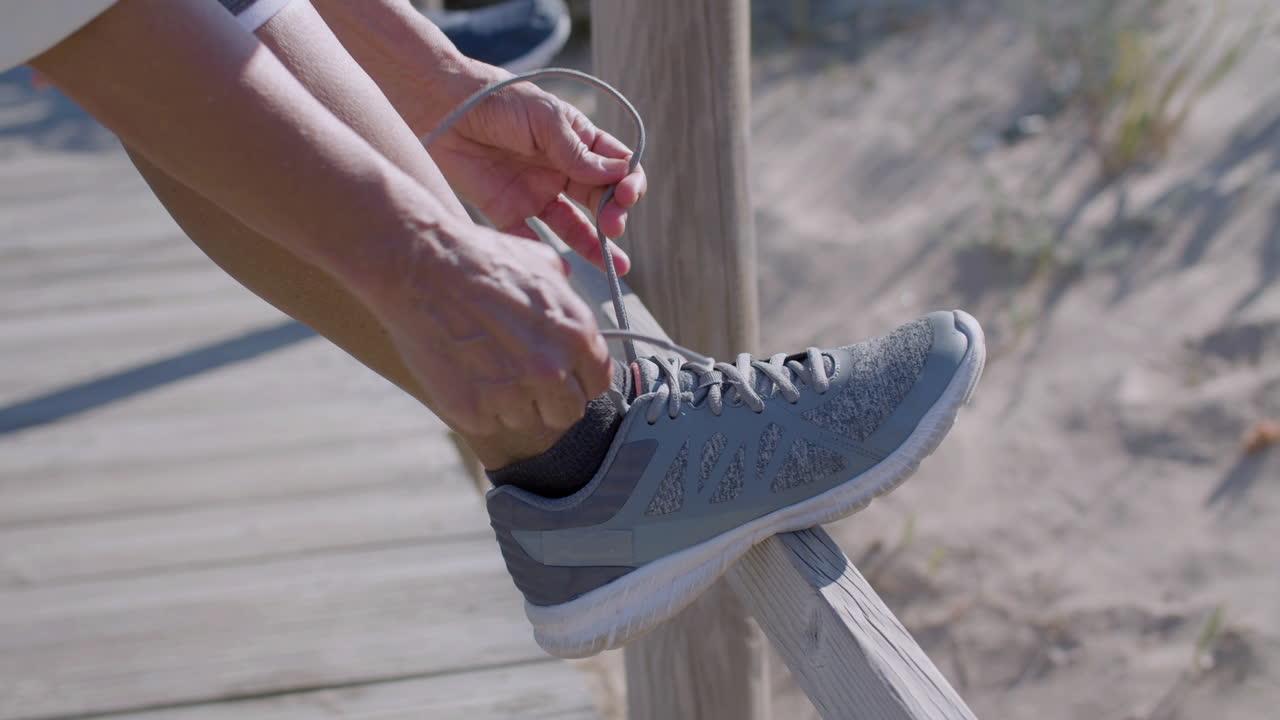 Donna matura irriconoscibile che si allaccia le scarpe da ginnastica in una giornata estiva