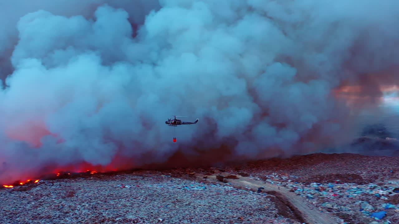 Aerial view of a Helicopter water drop on burning grasslands, African wildfires, in middle of thick smoke, dark evening, in South Africa - pan, drone shot