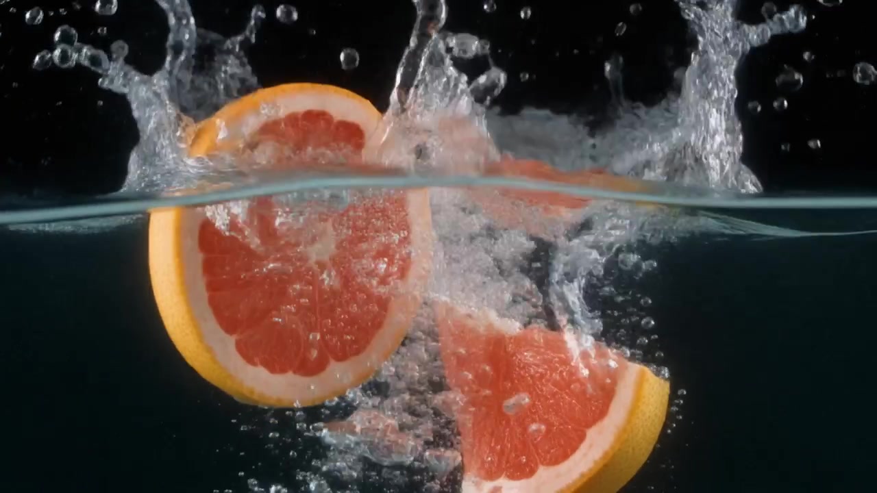 Fette di pompelmo che cadono nell'acqua con schizzi.