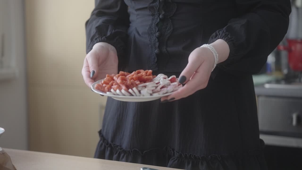 Girl in black dress presenting a plate with cheeses and salamis in a home kitchen setting
