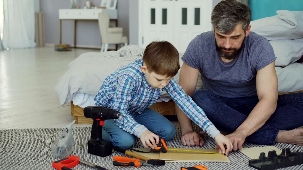 el niño pequeño está aprendiendo a usar el carrete de medición mientras hace trabajo de construcción con su padre, mientras que papá está explicando los fundamentos de la reparación y la construcción.