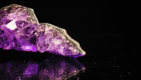 Elegant-macro-pan-of-purple-amethyst-crystal-lit-against-black-background,-with-reflection-below