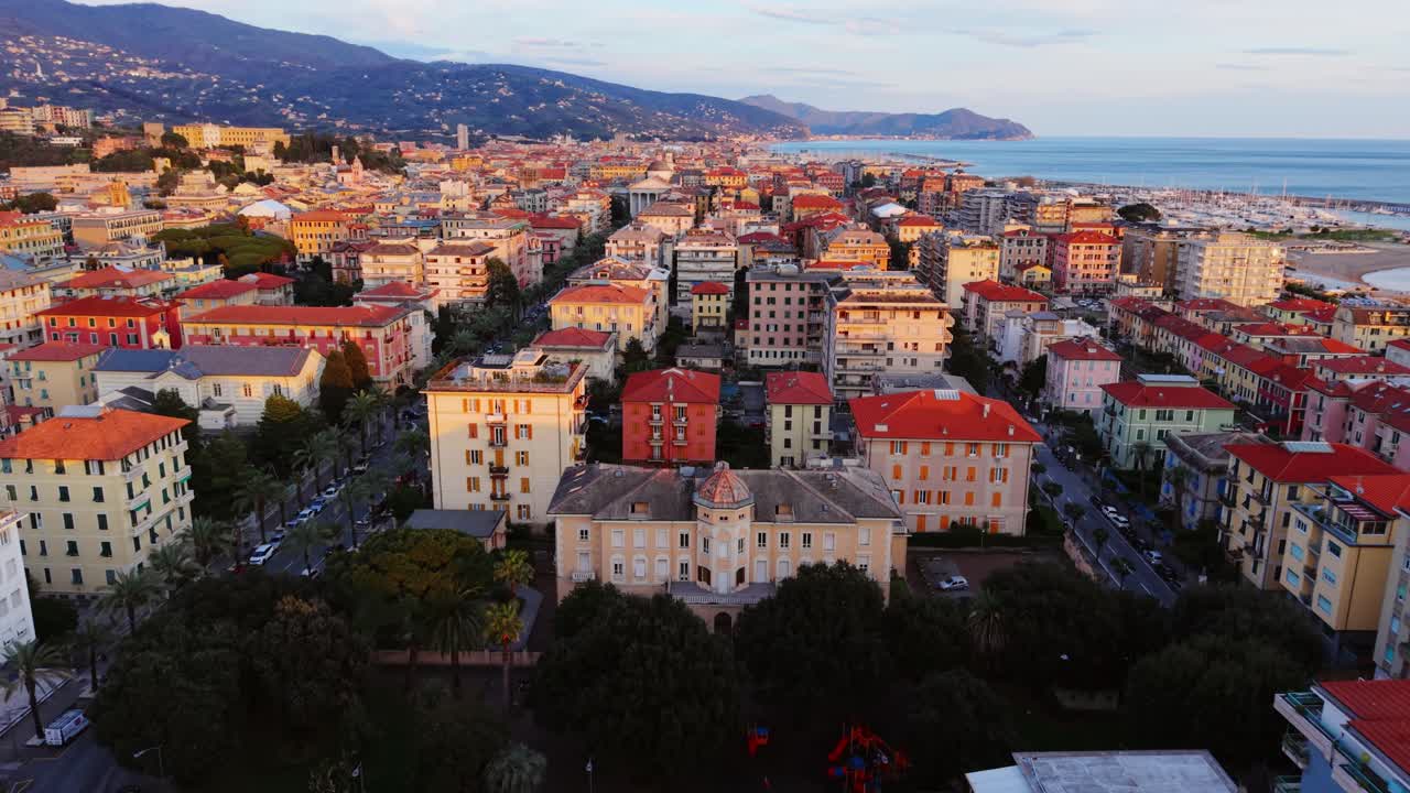 Coastal italian city with sea, sunset light, and mountain backdrop, aerial view