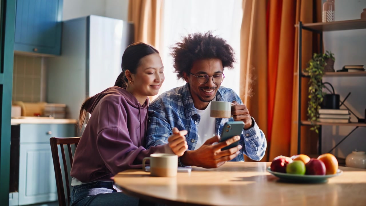 Coppia che naviga sullo smartphone in cucina durante la colazione. Coppia mista che condivide il caffè.