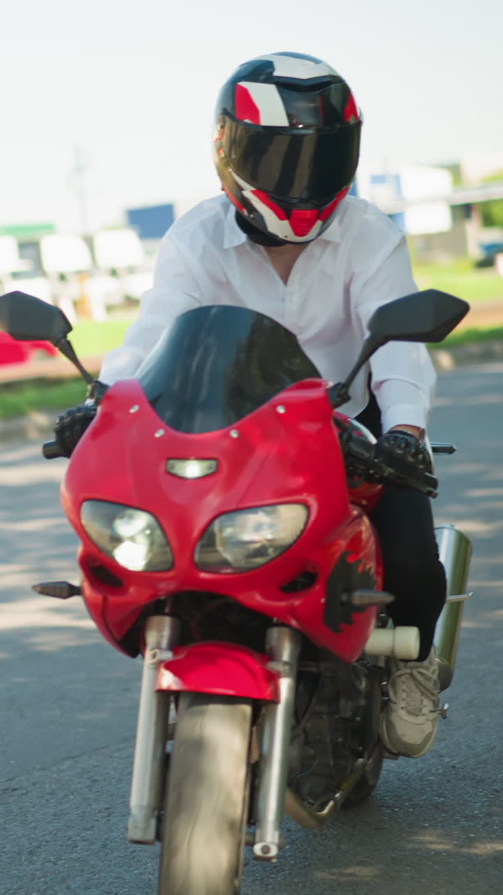 여성 오토바이 운전자가 빨간색 파워바이크를 타고 차 뒤에 차를 따라 그늘진 도로에서 회전하고, 다른 차는 도로를 가로질러 건물이 보입니다.