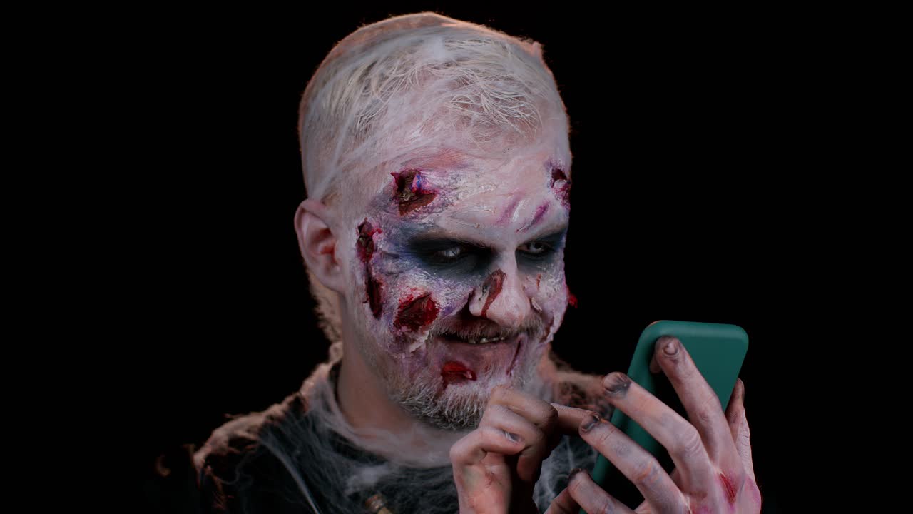 hombre aterrador halloween zombi usando teléfono móvil escribiendo nuevo post en la web, navegación, adicción