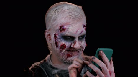 Hombre-Aterrador-Zombie-De-Halloween-Usando-Un-Teléfono-Móvil-Escribiendo-Una-Nueva-Publicación-En-La-Web,-Navegando,-Adicción