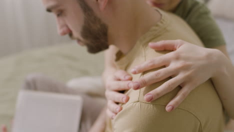 joven leyendo un libro mientras su novia lo abraza en el dormitorio