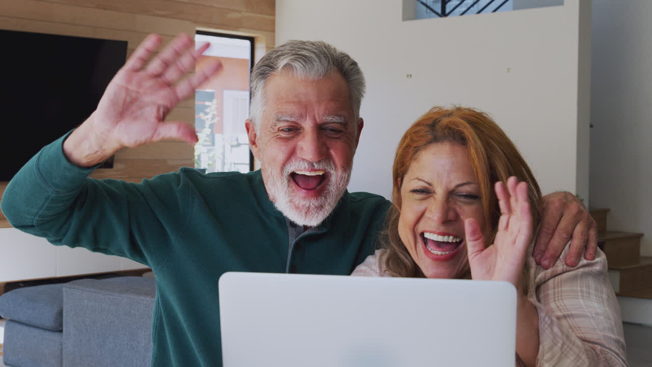 una pareja hispana senior en casa con una computadora portátil haciendo video chat con la familia.