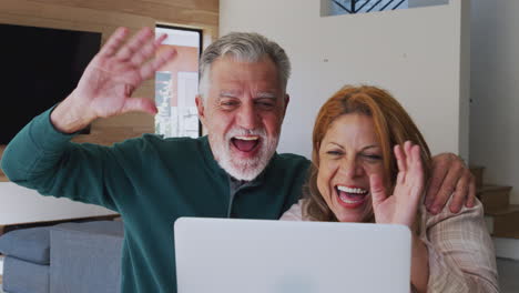 una pareja hispana senior en casa con una computadora portátil haciendo video chat con la familia.