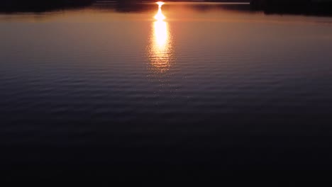 Filmische-Luftaufnahme-Eines-Atemberaubenden-Orangefarbenen-Sonnenuntergangs-über-Dem-Wasser-Des-Sees