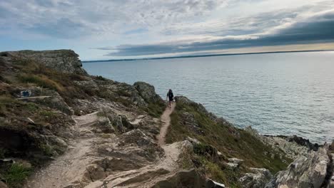 back view of young attractive hiker woman walking outdoors on top of mountain landscape with view on the ocean