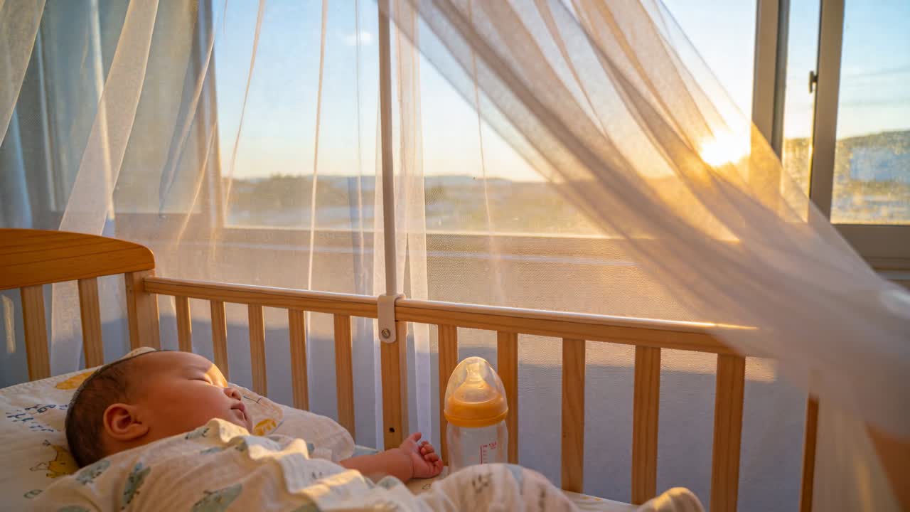 Neonato nella culla dell'asilo nido sdraiato vicino alla finestra, la brezza muove la tenda e fa sì che la mano cerchi il biberon.