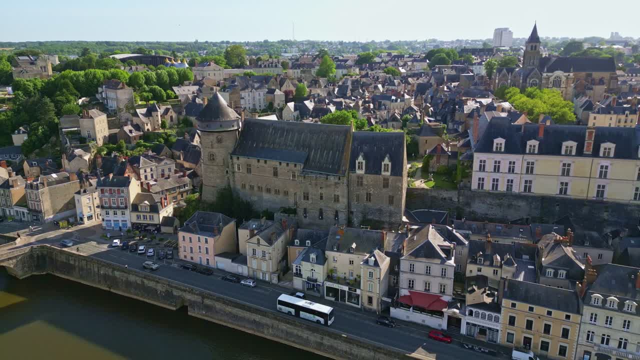 Drone pulls back from Laval Castle, revealing Mayenne riverbanks and the surrounding city under clear skies - Laval city in France