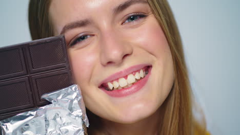 closeup young woman looking with chocolate bar at camera ion grey background.