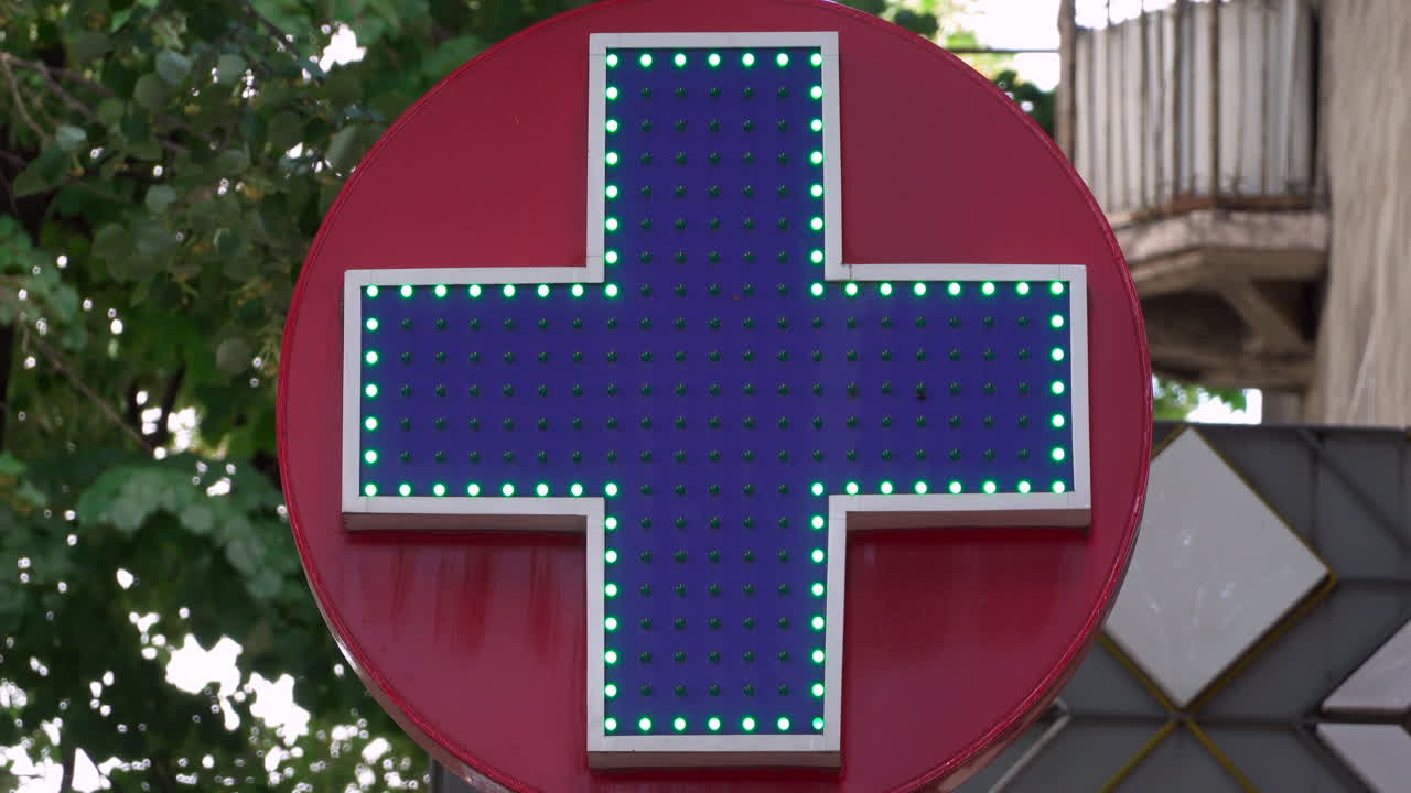 Cross pharmacy sign with trees and buildings on the background
