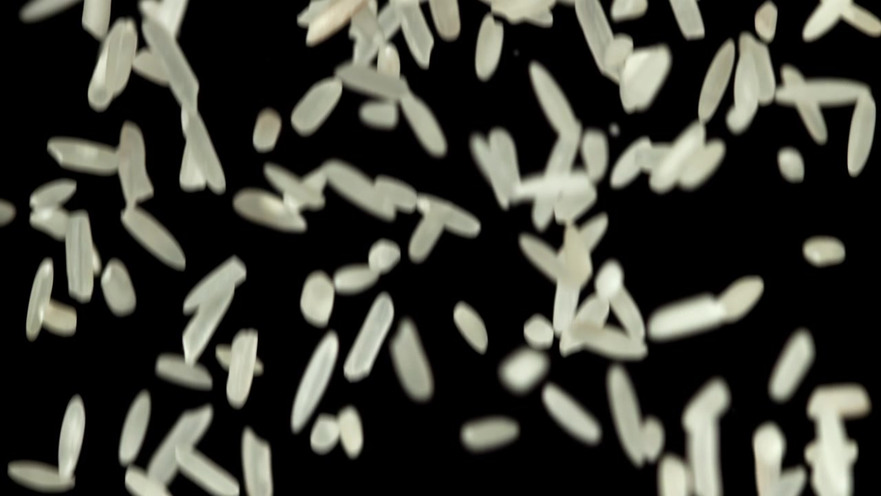 Ukogte hvide riskorn falder i slowmotion på sort baggrund