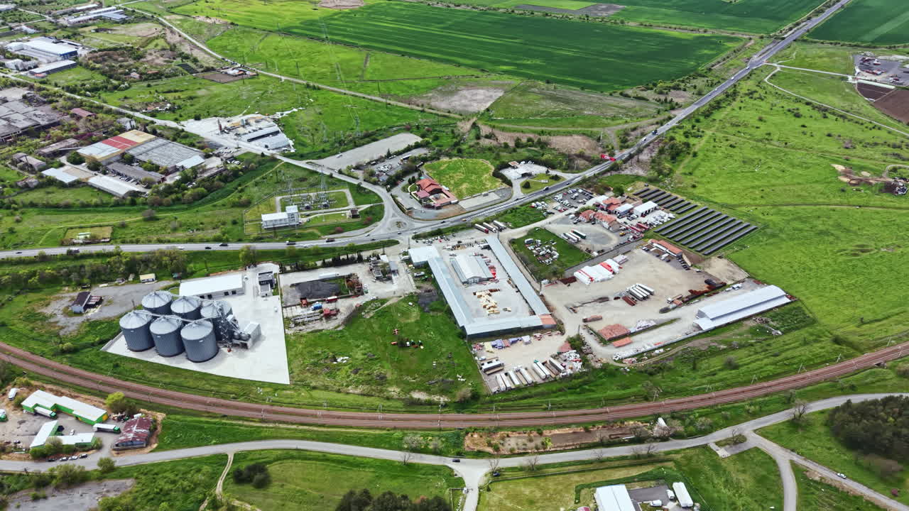 Aerial view of a rural area with fields, warehouses, and roads in daylight showing agricultural and industrial activities in a small community