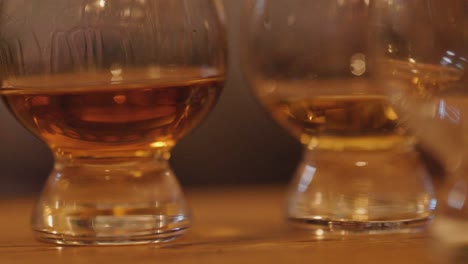 close-up of whiskey being gently swirled in a glass beside another, with warm ambient lighting and shallow depth of field on a wooden bar
