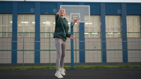 young girl practicing volleyball serve with basketball hoop and building in background, demonstrating sports technique on outdoor court