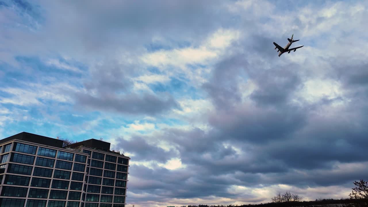 Airplane silhouette flying over modern building with dramatic cloudy sky, Prague